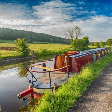 blue sky and green grass on the canal with a moored narrow boat